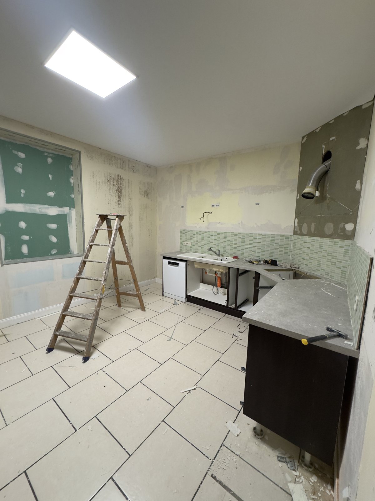 La cuisine pendant la dépose : anciens meubles démontés, faïence à nu, murs décollés et niche murale reconstruite en plaque hydrofuge.